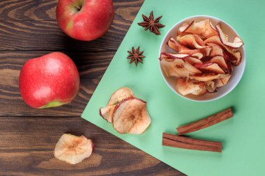 Elma cipslerinin, tarçınların ve kırmızı elmaların ahşap bir masada üst görüntüsü.