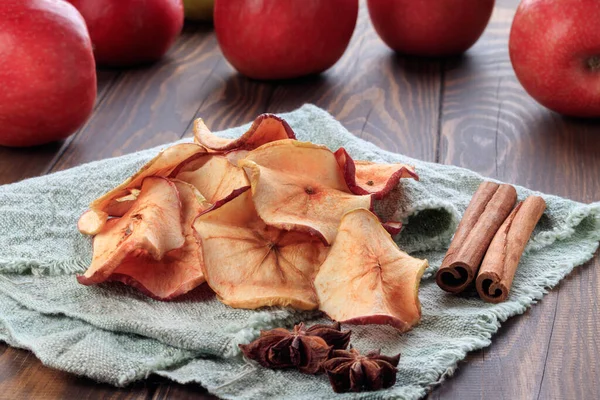 Heap of apple chips and cinnamon and red apples on background. Soft focus.