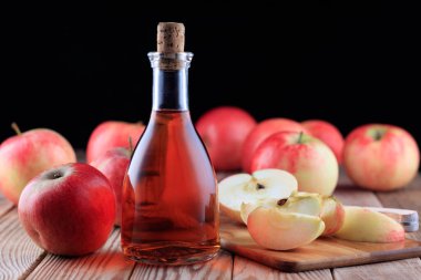 Ahşap arka planda bir şişe elma şarabı ve kırmızı elmalar. Yumuşak odak.