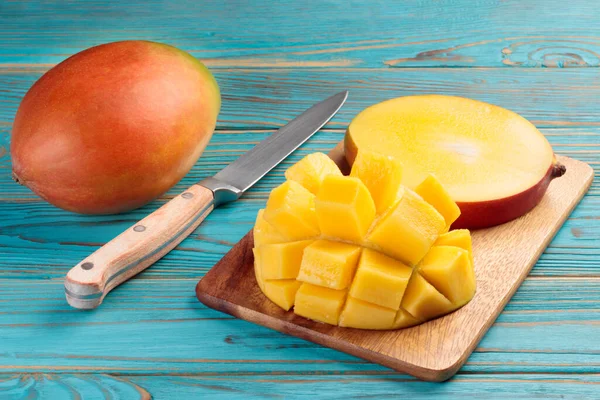 Kırsal bir masada, tahta bir tahtanın üzerinde bıçakla dilimlenmiş mango. Yumuşak odak.