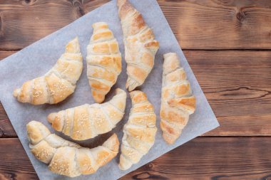 Top view of homemade croissants on a baking paper on wooden background. Horizontal orientation.