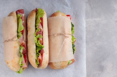 Üç tane Banh mi sandviçi, dilimlenmiş domuz eti, biber ve beyaz kağıda sarılmış salata. Kopyalama alanı ile.