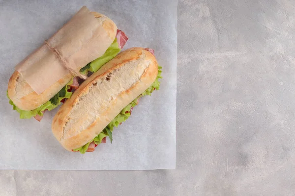 İki Banh mi sandviçi, dilimlenmiş domuz eti, biber ve beyaz kağıda sarılmış salata. Kopyalama alanı ile.