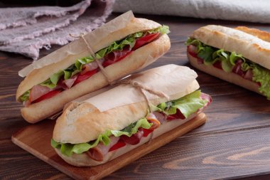 Dilimlenmiş domuz eti, biber ve ahşap arka planda kağıda sarılmış salatalı Banh mi sandviçi. Yumuşak odak.