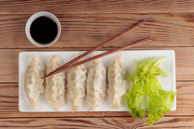 Dikdörtgen tabakta haşlanmış Çin mantısı, soya sosu ve ahşap arka planda yeşil salata..