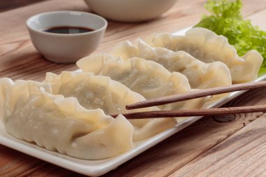 Dikdörtgen tabakta haşlanmış Çin hamur tatlısı, soya sosu ve ahşap arka planda yeşil salata. Yumuşak odak.