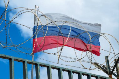 Rus bayrağının bulutlu gökyüzüne karşı dikenli tellerin arkasındaki görüntüsü. Kavram.