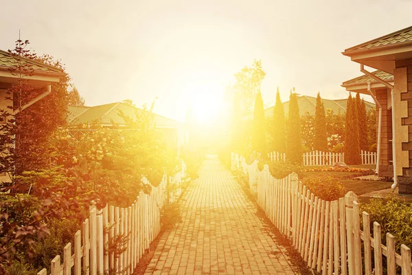 Sidewalk between cottages and gardens to rising sun.