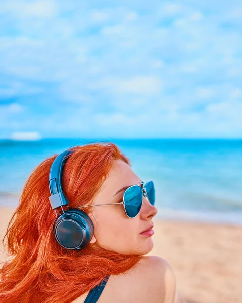 Belle femme en lunettes de soleil écoutant de la musique sur la plage. — Photo