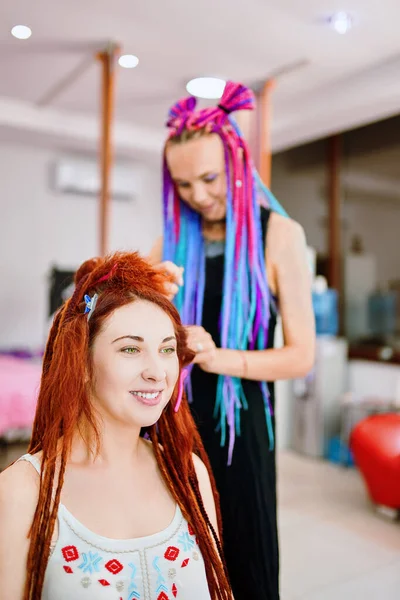 Hairdresser with colored afro braids weaves ginger dreadlocks. — Stock Photo, Image