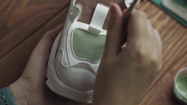Close up of females hands applies green acrylic paint on white sneaker — Stock Video