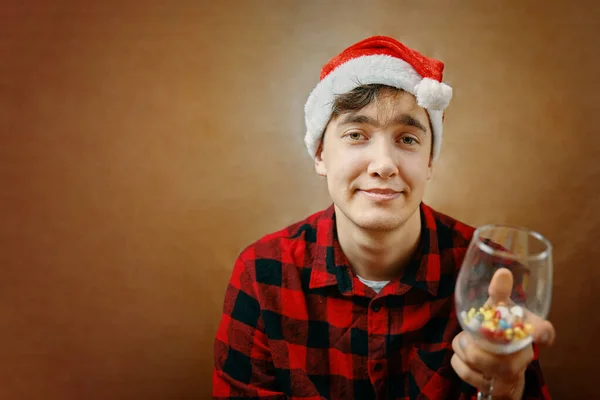 Guy in cappello di Babbo Natale tiene un bicchiere con varie pillole. — Foto Stock