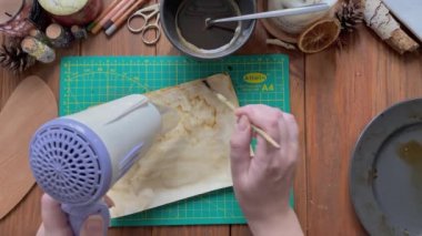 Sanatçı kağıdı su ve kahveyle süsleyip saç kurutma makinesiyle kurutuyor..