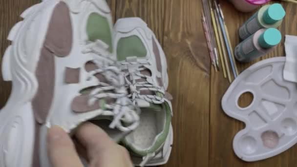 Személy kéz fog színes tornacipő és csavarja meg a kamera előtt. — Stock videók