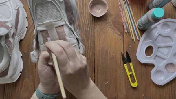 Flat lay of hands paint white boots with brush on wooden table. — Stock Video