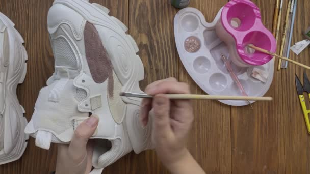 Womens hands paint sneakers with brush on wooden table. — Stock Video