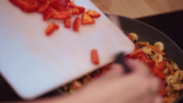 Повар наливает красный перец из доски в сковородку. — стоковое видео