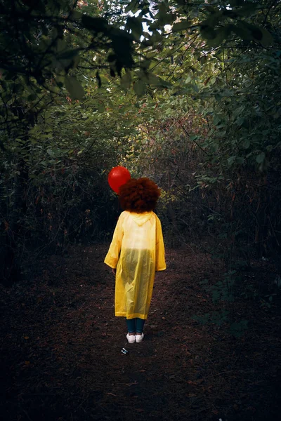 Donna in impermeabile giallo con un palloncino rosso sullo sfondo della foresta. — Foto Stock