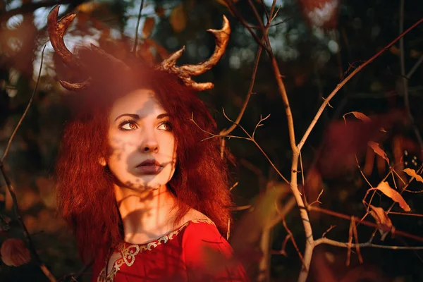 Donna in abito rosso lungo con corna di cervo nella foresta autunnale. — Foto Stock