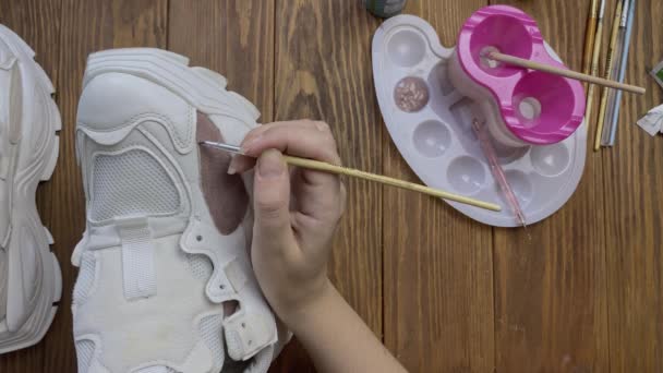 Top view of hands paint white boots with brush on wooden table. — Stock Video