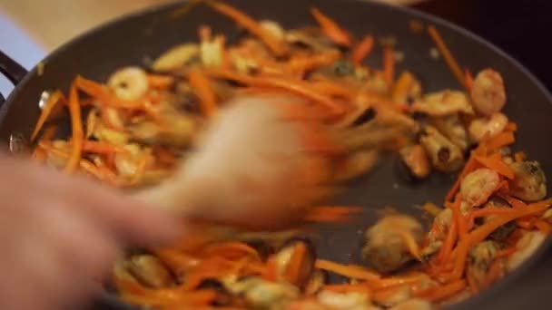 Повар смешивает ингредиенты в сковороде с деревянной ложкой. — стоковое видео