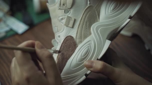 Artist paints white sneakers on wooden table. — Stock Video