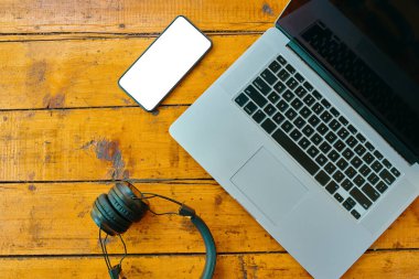 Dizüstü bilgisayar, kablosuz kulaklık ve cep telefonu ahşap masada..