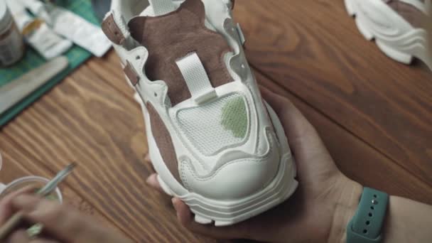 Woman artist applies green acrylic paint on white sneaker with brush. — Stock Video