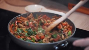 Ahşap kaşıkla şefin eli kızartma tavasındaki malzemeleri karıştırır..