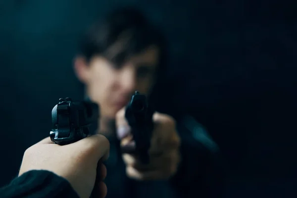 Close-up of mans hand with gun pointed at criminal with revolver.