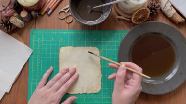 Dişilerin elleri, el sanatları kağıdını su ve kahve solüsyonuyla süsler..