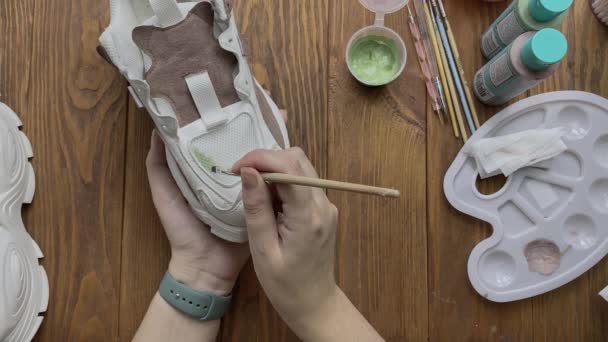 Woman drawing on white boots with brush on desktop. — Stock Video