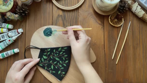 Дівчина малює листя на медичній масці з пензлем і фарбою . — стокове відео