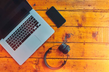 Dizüstü bilgisayar, kablosuz kulaklık ve cep telefonu ahşap masada..