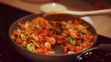 Kızartma tavasındaki malzemeleri ahşap kaşıkla kadınlar karıştırır..