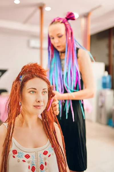 Hairdresser with colored afro braids weaves ginger dreadlocks. — Stock Photo, Image