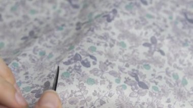 Kadınların elleri çiçek kumaşından bir parça kesiyor dikiş makası ile.
