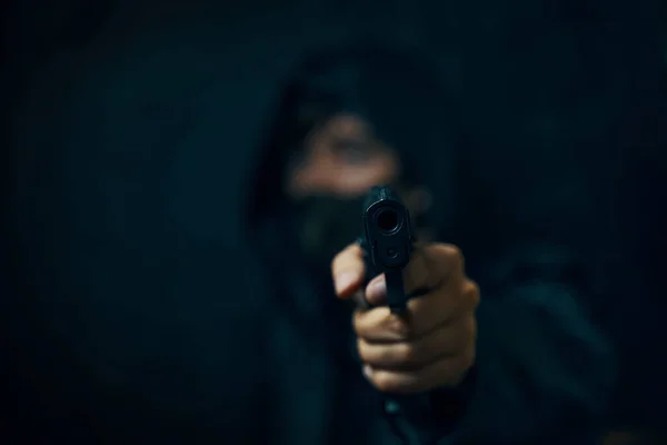 Man i huva och mask hotar med skjutvapen. — Stockfoto