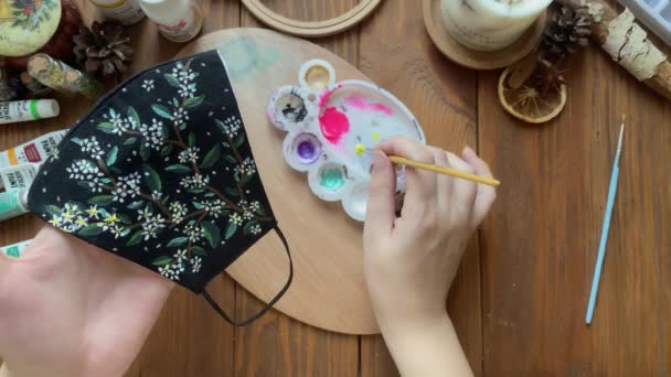 Kobieta rysować liście i kwiaty na medycznej masce tkaniny z pędzlem. — Wideo stockowe