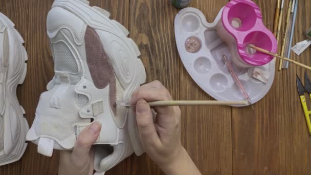人们用手把刷子蘸到褐色的油漆中，然后用它来做运动鞋. — 图库视频影像