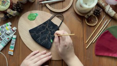 Elleri, kumaş maskesine akrilik boyalarla yapraklar çizer..