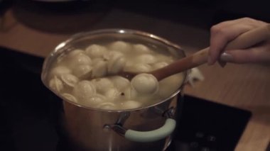 Kadın cam seramik mutfak sobasında alüminyum tavada pelmeni pişiriyor.