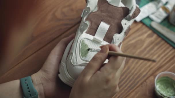 Artista femenina aplica pintura acrílica verde en zapatillas blancas con pincel. — Vídeos de Stock