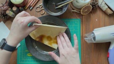 Female artist hands dipping piece of paper into plate of coffee.