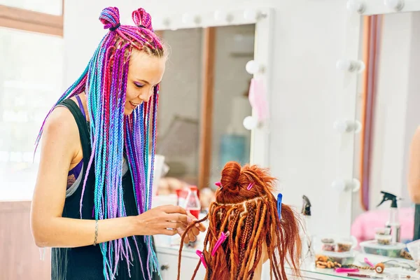 Γυναίκα κομμωτήριο υφαίνει στο κορίτσι dreadlocks τζίντζερ. — Φωτογραφία Αρχείου