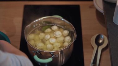 Kadın cam seramik mutfak sobasında alüminyum tavada pelmeni pişiriyor.