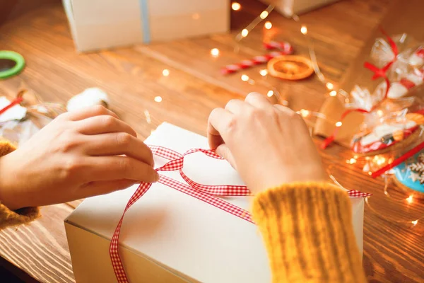 Frauenhände Strickpullovern Binden Rote Schleifen Auf Weißem Geschenkkarton Neujahrsstimmung Lichterketten — Stockfoto