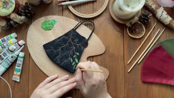 Людина малює листя на медичній масці з пензлем і фарбою . — стокове відео