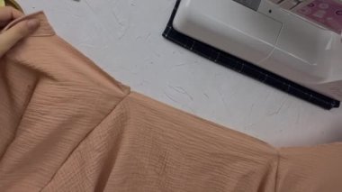 Terzi elleri birbirlerine pamuklu kumaş gömleğin detaylarını anlatmaya çalışırlar. Bluzun yakası iğnelerle bağlanmış. Moda tasarımcılığının işyeri. Dikiş makinesi ve diğer araçlar beyaz desenli tablo üzerinde.