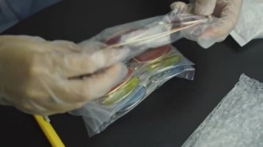 Eldivenli insanlar plastik torbalardan kırmızı bardakları çıkarır ve onları gösterir. Kabarcık ambalajı, güneş gözlüğü seti ve siyah masada duran bıçak. Yaz için yeni moda aksesuarları açıyorum..